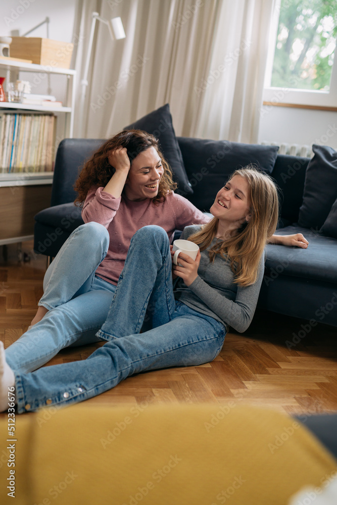 Dwie kobiety siedzące na podłodze w salonie, rozmawiające i uśmiechnięte.