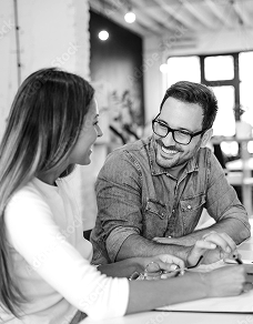 Kobieta i mężczyzna siedzący przy stole, uśmiechają się do siebie podczas rozmowy.