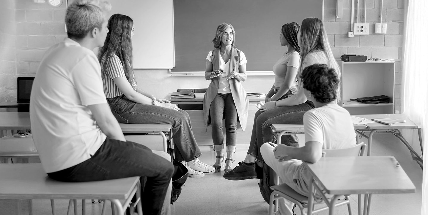 Nauczycielka prowadzi rozmowę z grupą uczniów w klasie.